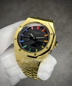 Modern timepiece with a gold-colored stainless steel bracelet, a minimalist black dial, and a distinctive rainbow hour index design.