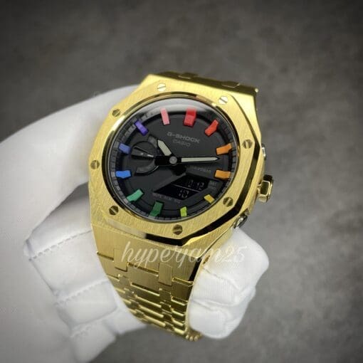 Modern timepiece with a gold-colored stainless steel bracelet, a minimalist black dial, and a distinctive rainbow hour index design.
