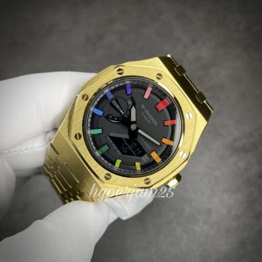 Close-up of a luxurious gold stainless steel watch with a sleek black dial and custom rainbow-colored hour indicators.